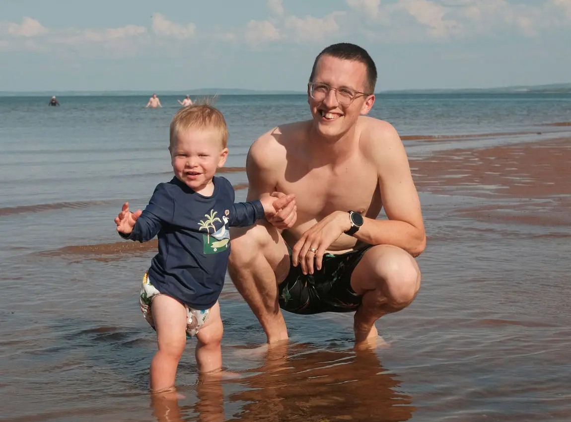 Cadel crouching on the beach beside his child